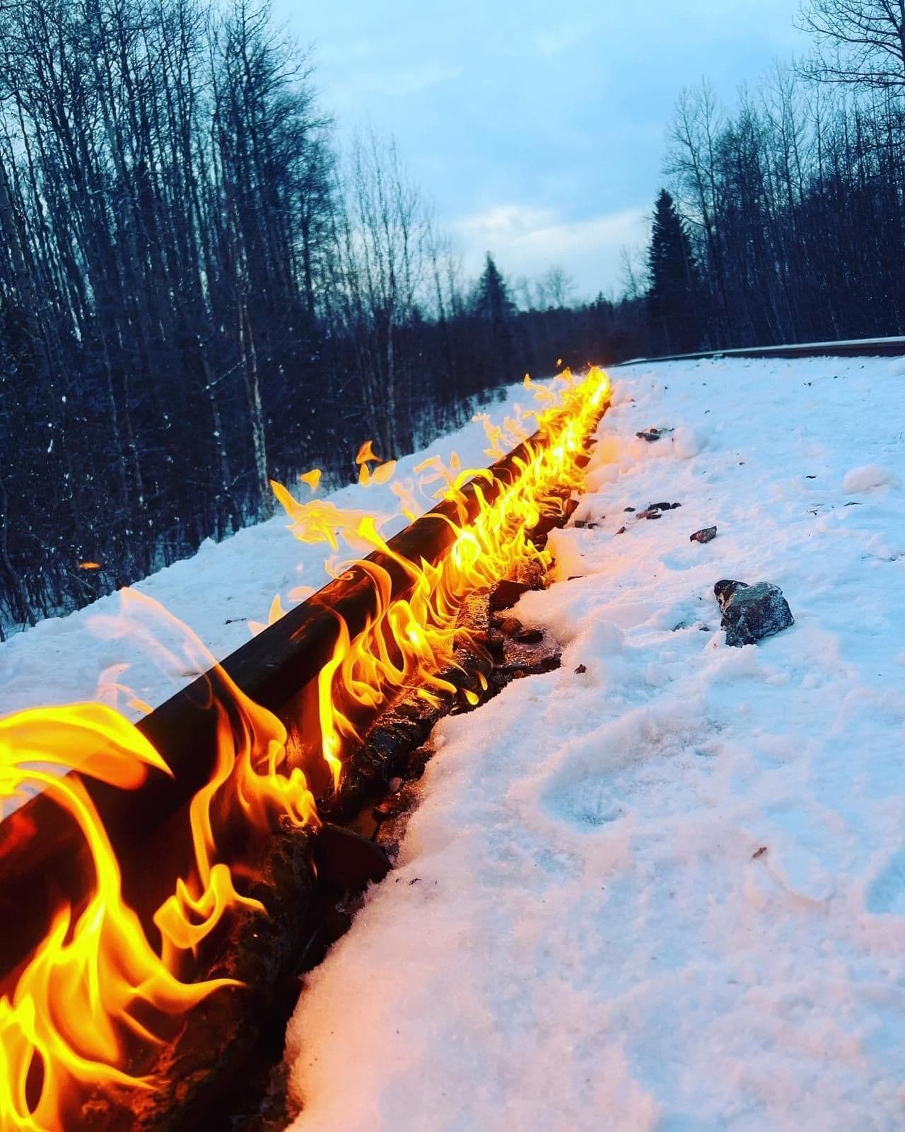 Flames burning along a rail through deep snow beside a forest