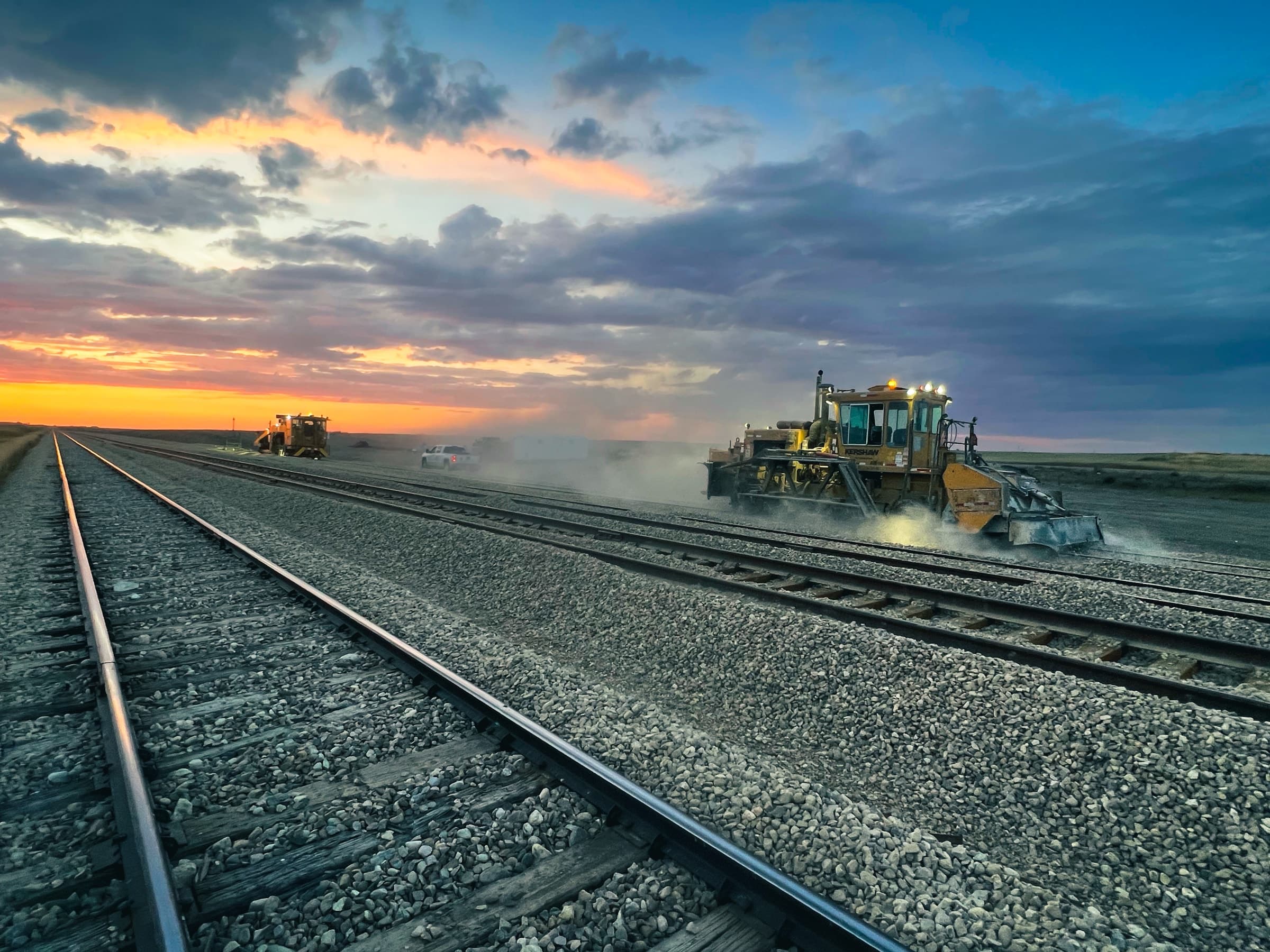 Railway surfacing equipment working beside track at sunset